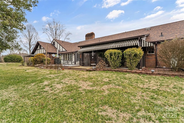 back of house with a deck, brick siding, a yard, roof with shingles, and a chimney