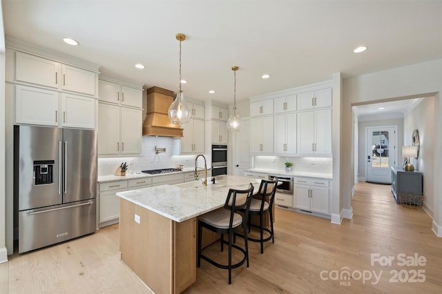 kitchen featuring backsplash, a sink, custom exhaust hood, light wood-style floors, and stainless steel appliances