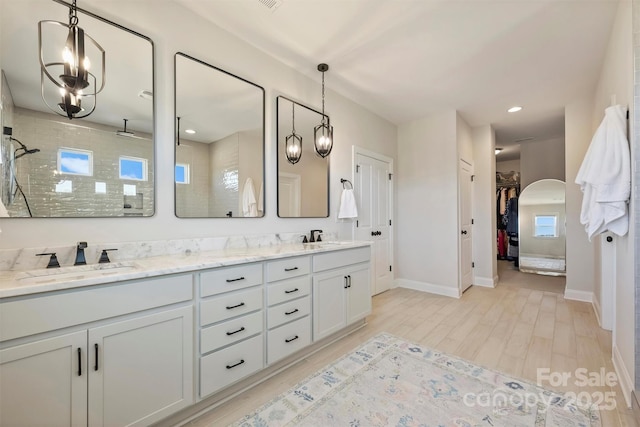 full bathroom featuring double vanity, a walk in closet, a tile shower, wood finished floors, and a sink