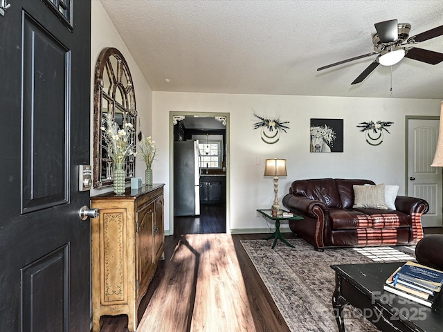 living area with ceiling fan, baseboards, dark wood-style flooring, and a textured ceiling