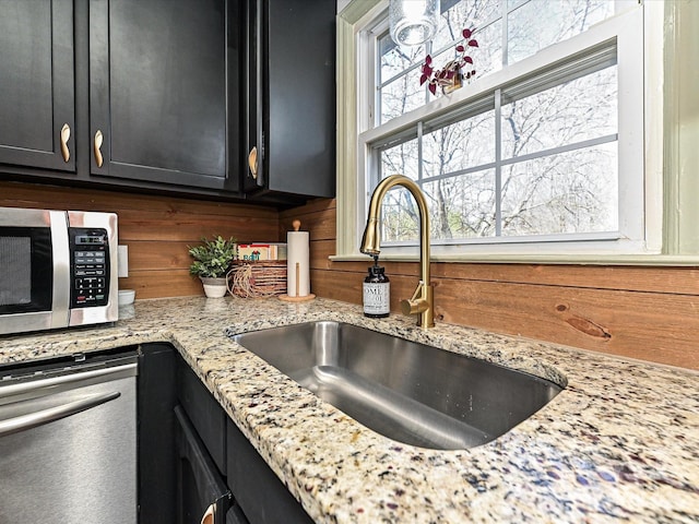 interior details with stainless steel microwave, light stone countertops, dark cabinets, and a sink