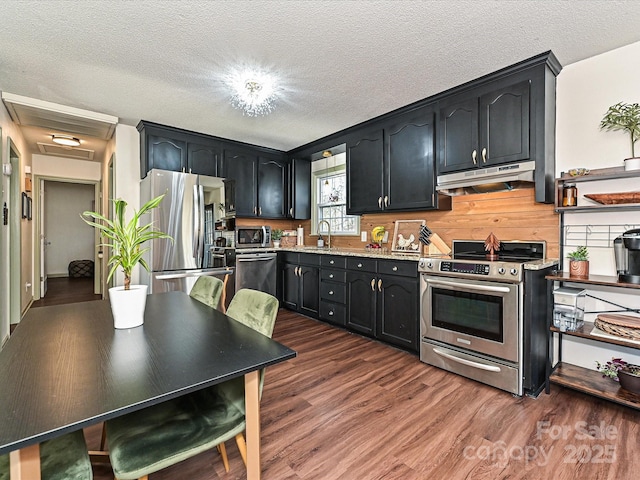 kitchen with under cabinet range hood, appliances with stainless steel finishes, dark wood-style floors, a textured ceiling, and a sink