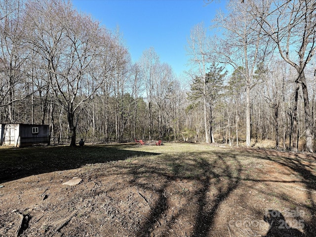 view of yard featuring an outbuilding, a storage unit, and a wooded view