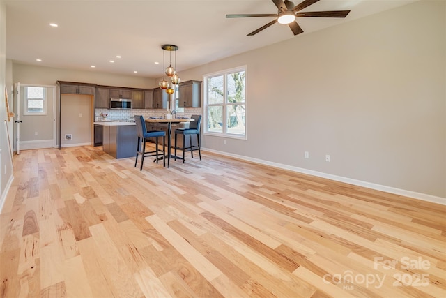 kitchen featuring stainless steel microwave, backsplash, light countertops, a kitchen breakfast bar, and light wood-style floors