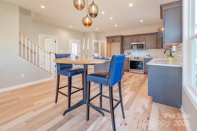 kitchen featuring light countertops, decorative backsplash, light wood-style flooring, stainless steel appliances, and a sink