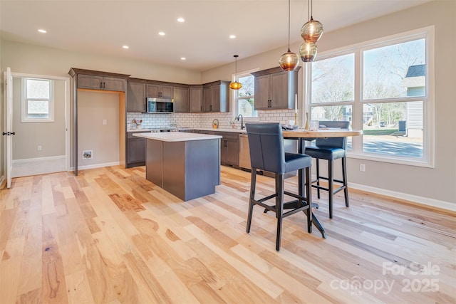 kitchen with light wood-style flooring, tasteful backsplash, appliances with stainless steel finishes, and a kitchen island