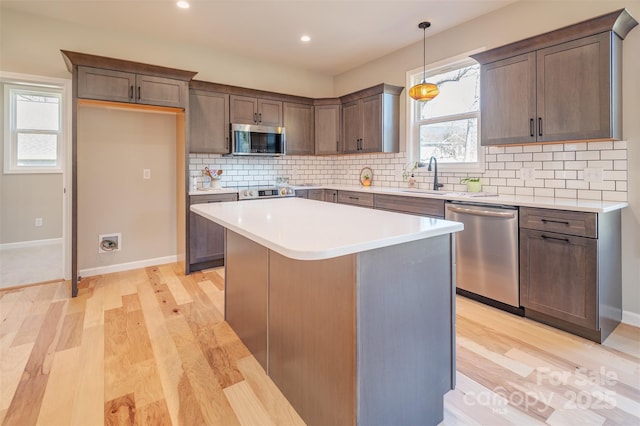 kitchen with light wood finished floors, decorative backsplash, appliances with stainless steel finishes, and a sink