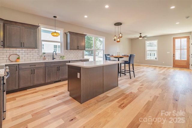 kitchen with backsplash, a kitchen island, light countertops, light wood-style flooring, and a sink