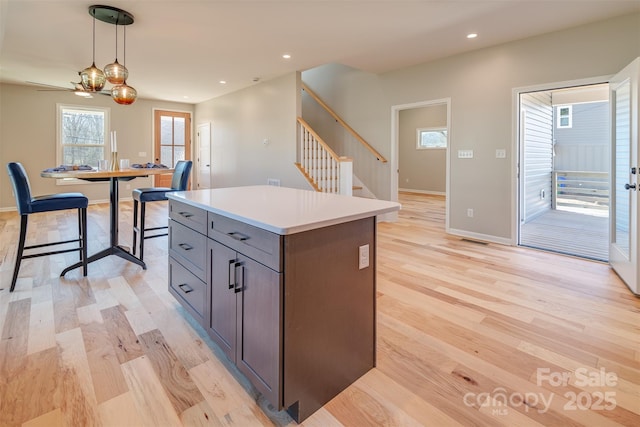 kitchen with light wood-style flooring, a kitchen island, recessed lighting, light countertops, and hanging light fixtures