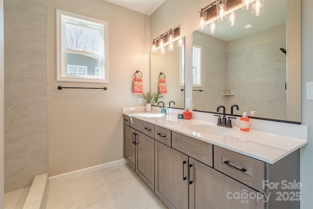 full bath featuring double vanity, tiled shower, baseboards, and a sink