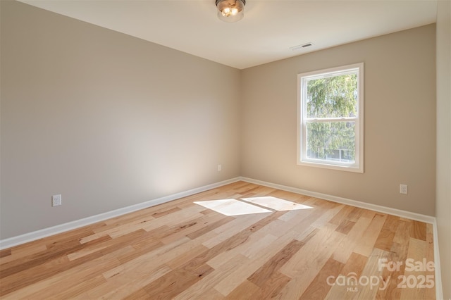 spare room featuring light wood-type flooring, visible vents, and baseboards