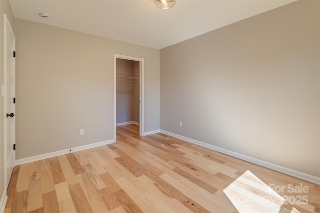 unfurnished bedroom featuring a walk in closet, light wood-style floors, baseboards, and a closet