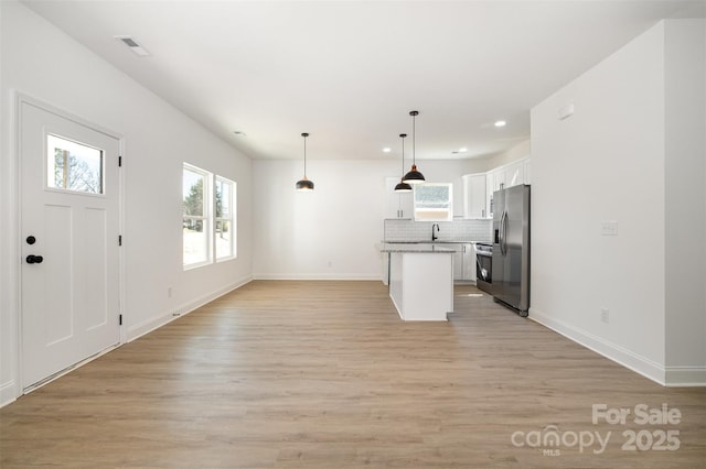 kitchen with backsplash, open floor plan, white cabinetry, a sink, and stainless steel fridge