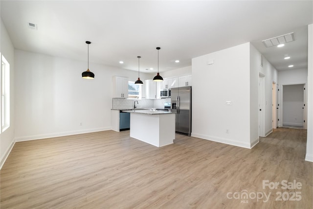 kitchen featuring stainless steel appliances, a kitchen island, visible vents, light wood-type flooring, and decorative backsplash