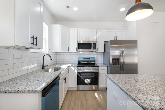 kitchen featuring stainless steel appliances, a sink, white cabinets, light wood-style floors, and backsplash