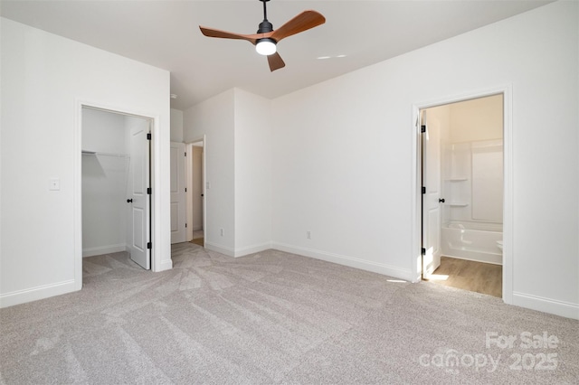 unfurnished bedroom with baseboards, a closet, a walk in closet, carpet, and ensuite bath