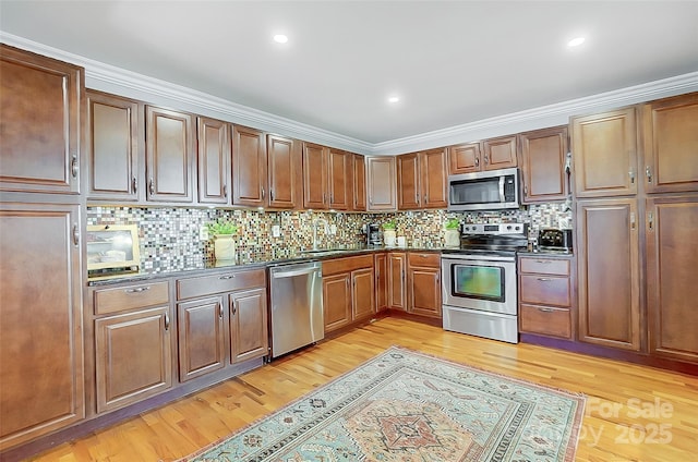 kitchen featuring light wood finished floors, stainless steel appliances, dark countertops, backsplash, and a sink