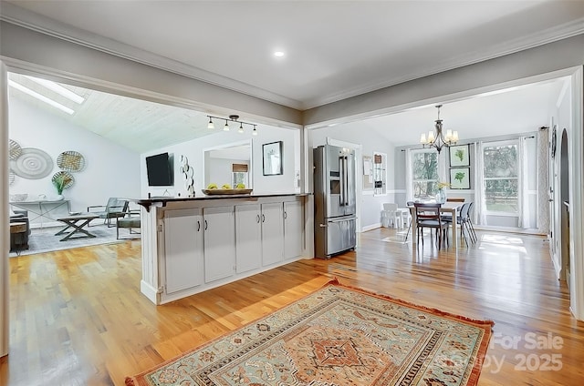 kitchen featuring high quality fridge, a peninsula, vaulted ceiling, light wood-style floors, and a notable chandelier