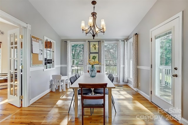 dining area with light wood-style floors, baseboards, vaulted ceiling, and an inviting chandelier