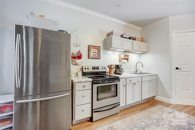 kitchen with light stone counters, stainless steel appliances, a sink, ornamental molding, and light wood-type flooring