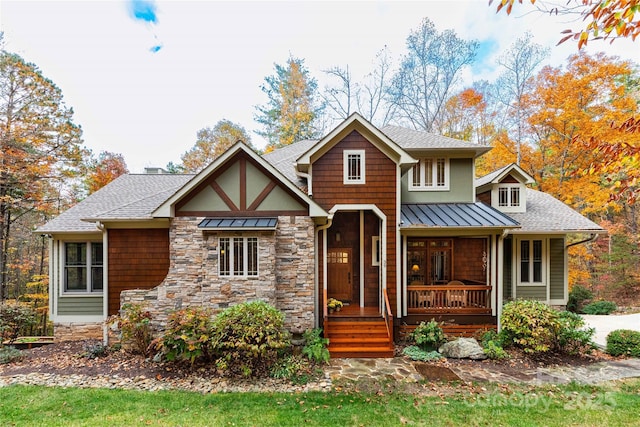 view of front of property with a standing seam roof, stone siding, a porch, roof with shingles, and metal roof