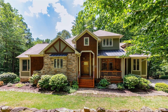 view of front of property featuring a standing seam roof, stone siding, covered porch, a shingled roof, and metal roof