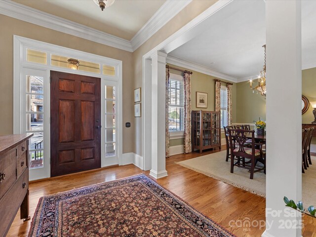 foyer featuring ornamental molding, wood finished floors, decorative columns, and an inviting chandelier