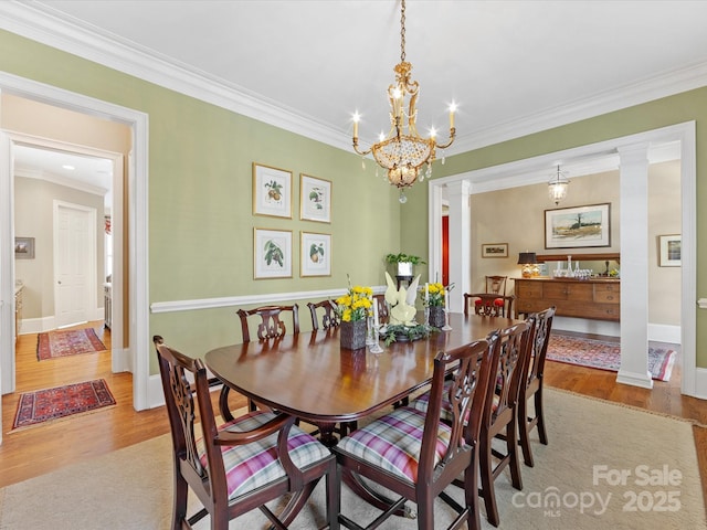 dining space featuring crown molding, decorative columns, wood finished floors, a chandelier, and baseboards