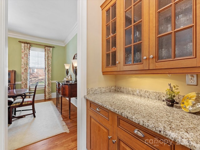 kitchen featuring brown cabinets, light wood-style flooring, ornamental molding, light stone countertops, and baseboards