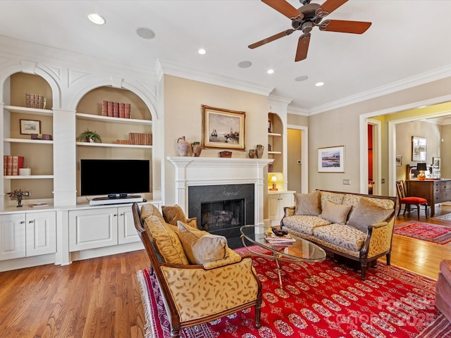 living room featuring ornamental molding, built in shelves, light wood finished floors, and a premium fireplace