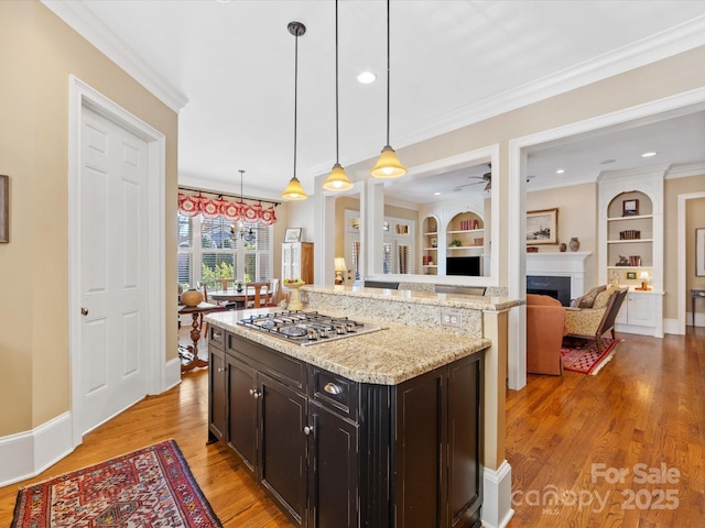 kitchen featuring crown molding, a fireplace, stainless steel gas cooktop, light stone countertops, and light wood-type flooring