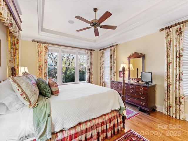 bedroom featuring baseboards, a raised ceiling, ceiling fan, light wood-style flooring, and crown molding