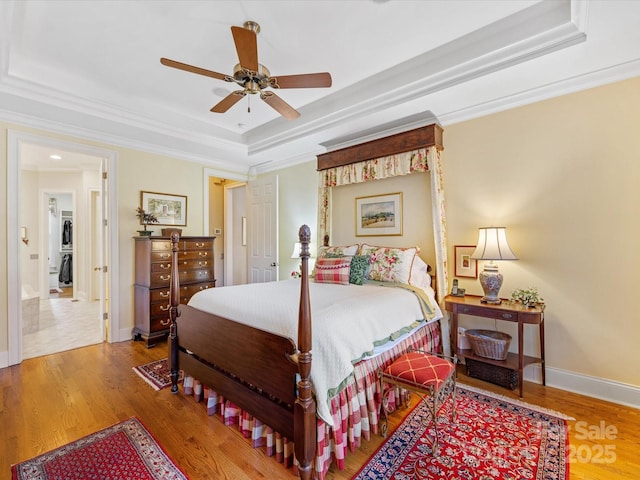 bedroom featuring wood finished floors, a ceiling fan, baseboards, ornamental molding, and a raised ceiling