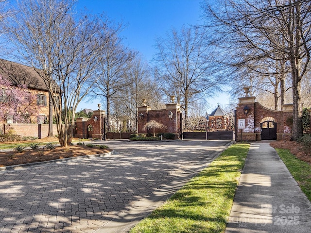 view of road with street lighting, a gate, sidewalks, a gated entry, and curbs