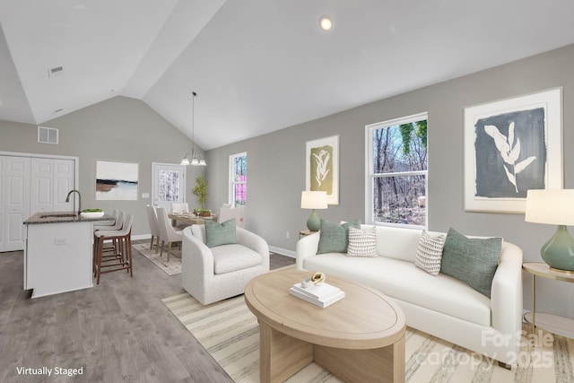 living area with a notable chandelier, wood finished floors, visible vents, baseboards, and vaulted ceiling