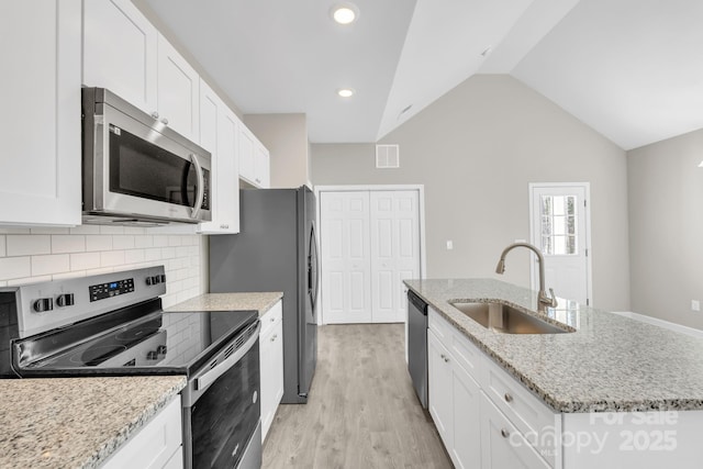 kitchen with vaulted ceiling, appliances with stainless steel finishes, a sink, and white cabinetry