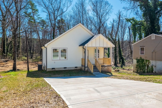 view of front of home with board and batten siding, crawl space, covered porch, a wooded view, and a front yard