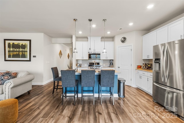 kitchen featuring a kitchen breakfast bar, backsplash, dark wood-style floors, appliances with stainless steel finishes, and light countertops