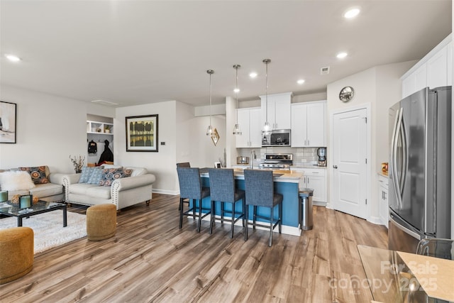 kitchen featuring open floor plan, a breakfast bar, light wood-style floors, white cabinets, and stainless steel appliances