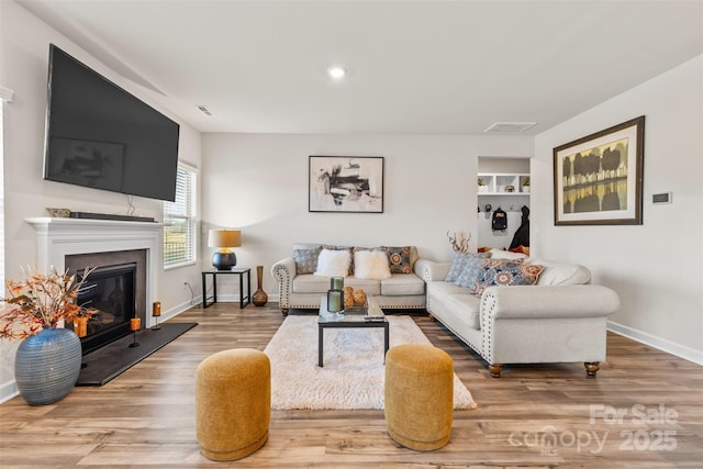 living room with wood finished floors, visible vents, baseboards, recessed lighting, and a glass covered fireplace