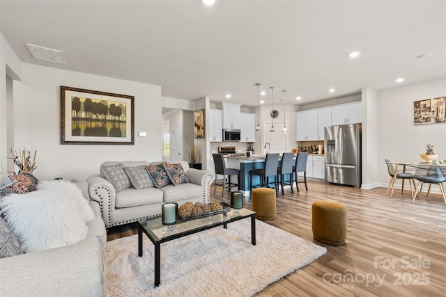 living room featuring recessed lighting, light wood-type flooring, baseboards, and visible vents