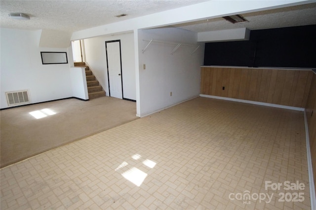 finished below grade area featuring carpet floors, stairway, visible vents, and a textured ceiling