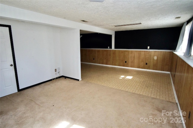 spare room featuring visible vents, wainscoting, light colored carpet, a textured ceiling, and wood walls