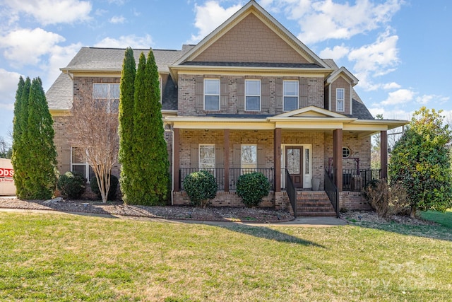 view of front of house featuring covered porch, brick siding, roof with shingles, and a front yard