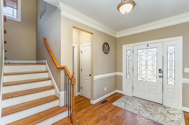 foyer entrance with crown molding, visible vents, wood finished floors, baseboards, and stairs