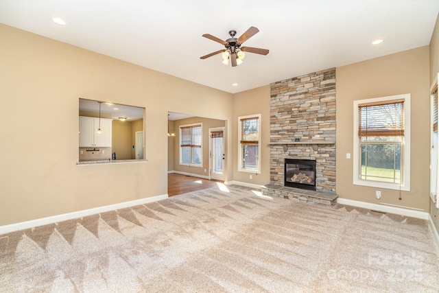 unfurnished living room with carpet floors, a wealth of natural light, a stone fireplace, and baseboards