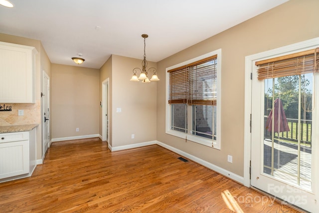 unfurnished dining area featuring a notable chandelier, light wood-style flooring, visible vents, and baseboards