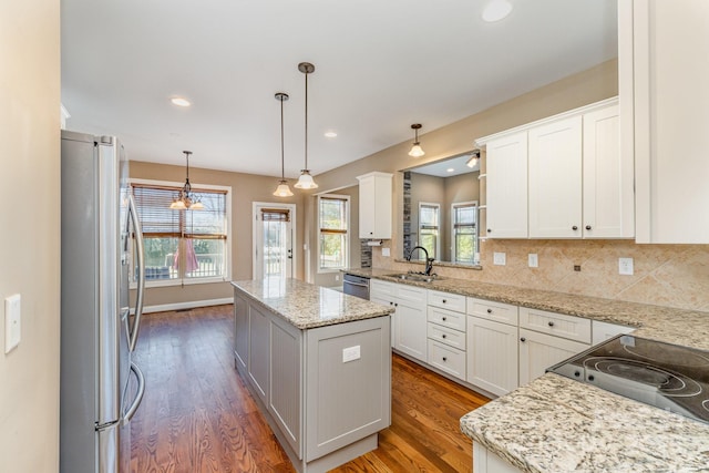 kitchen featuring wood finished floors, a kitchen island, a sink, appliances with stainless steel finishes, and tasteful backsplash