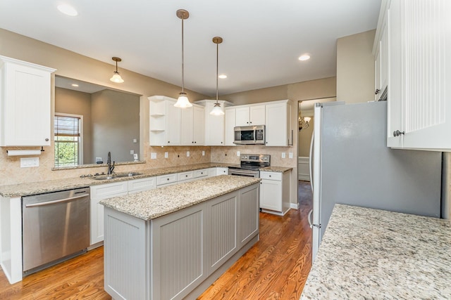 kitchen featuring appliances with stainless steel finishes, a center island, a sink, light wood-style floors, and backsplash