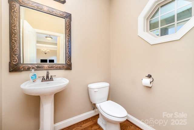 half bathroom featuring baseboards, a sink, toilet, and wood finished floors